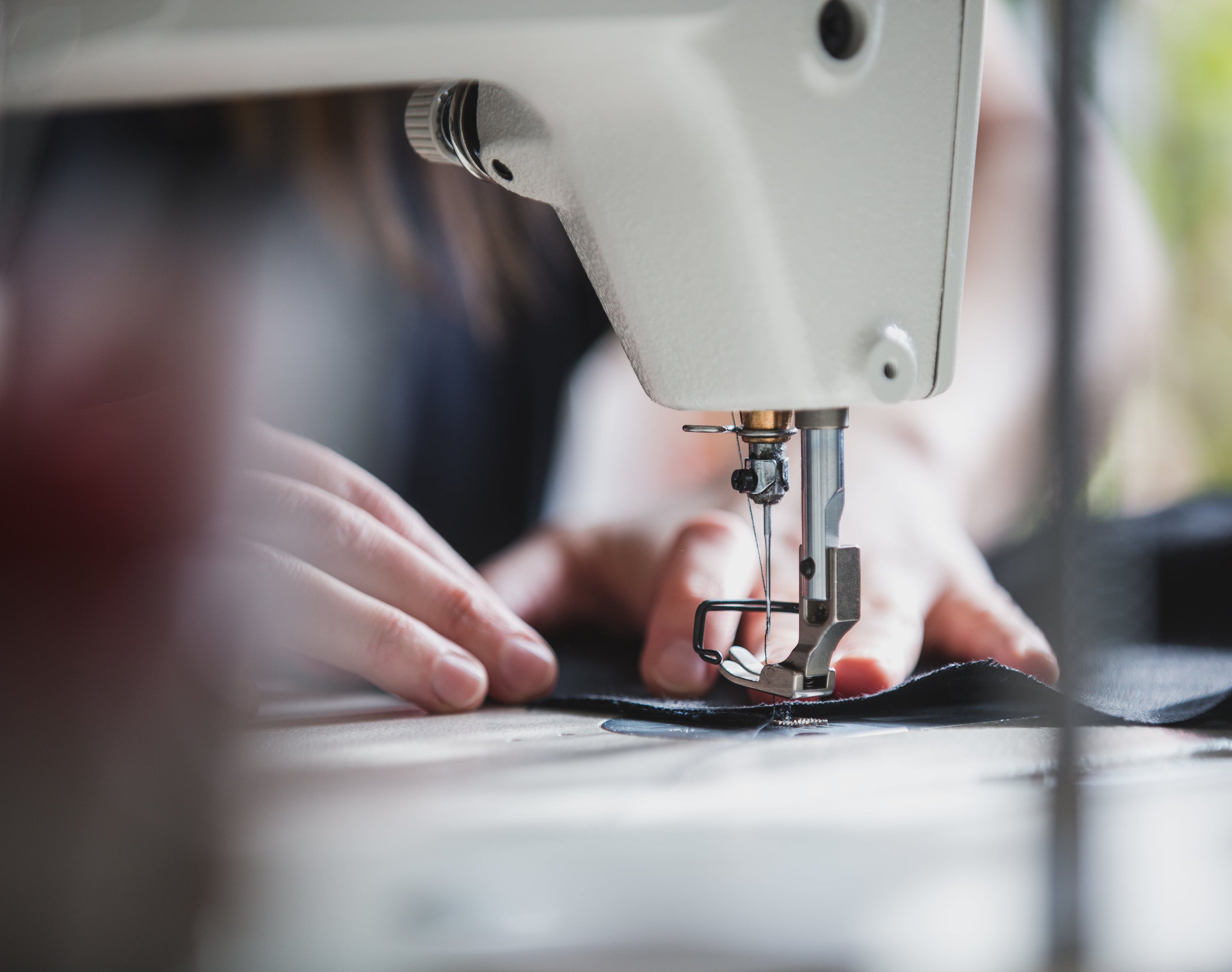 A close-up shot of a person's hands guiding fabric under the needle of a white sewing machine.